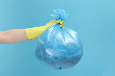 Açık mavi arka planda çöp dolu plastik poşet taşıyan kadın, yakın plan.