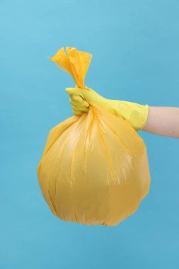 Açık mavi arka planda çöp dolu plastik poşet taşıyan kadın, yakın plan.