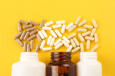 Sarı zemin üzerinde şişeler ve farklı vitamin kapsülleri, düz yatış