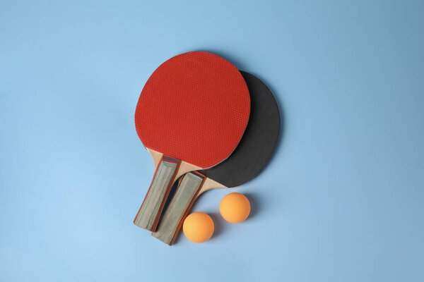 Ping pong balls and rackets on light blue background, flat lay