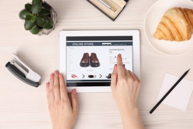 Tabletli bir kadın beyaz ahşap masada internetten alışveriş yapıyor.