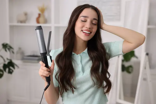 Happy woman with curling hair iron at home