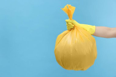 Açık mavi arka planda çöp dolu plastik poşet taşıyan bir kadın, yakın plan. Metin için boşluk