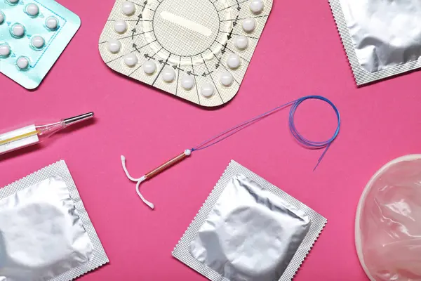 Contraceptive pills, condoms, intrauterine device and thermometer on pink background, flat lay. Different birth control methods