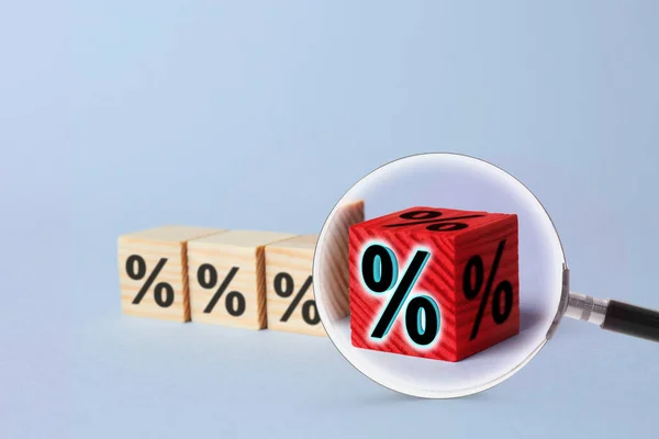 Best mortgage interest rate. Red cube with percent sign among wooden ones on light background, view through magnifying glass