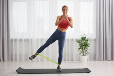Spor yapan atletik bir kadın evde spor yaparken lastikli bant takıyor.