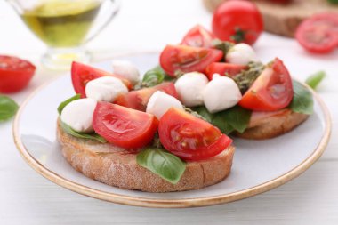Mozzarella, domates, fesleğen ve pesto soslu leziz Caprese sandviçleri beyaz ahşap masada, yakın plan.