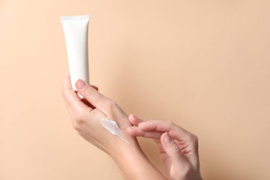 Bej arka planda eline kozmetik krem süren bir kadın, yakın plan. Metin için boşluk
