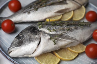 Çiğ dorado balığı kekik, limon dilimleri ve domatesler masada, yakın plan.