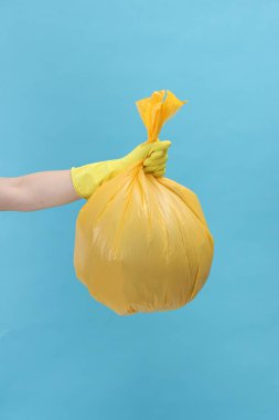 Açık mavi arka planda çöp dolu plastik poşet taşıyan kadın, yakın plan.