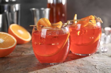 Aperol sprey kokteyli, buz küpleri ve portakal dilimleri gri desenli masada, yakın plan.