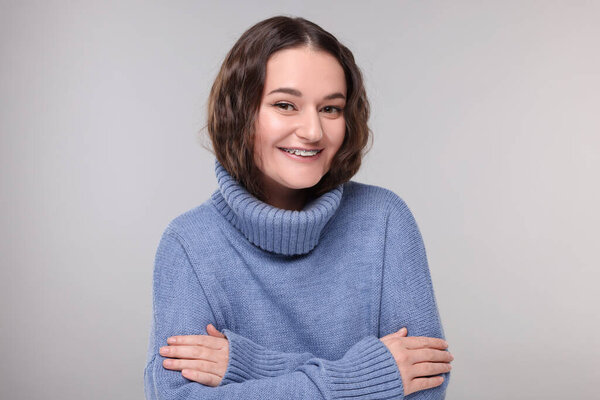 Smiling woman with dental braces in warm sweater on grey background