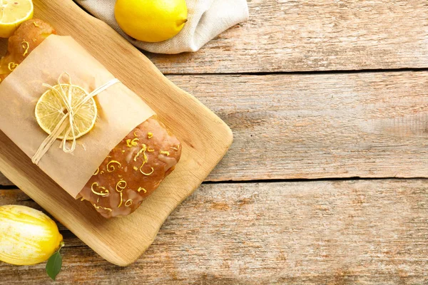 Wrapped tasty lemon cake with glaze and citrus fruits on wooden table, flat lay. Space for text