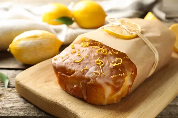 Wrapped tasty lemon cake with glaze on wooden table, closeup