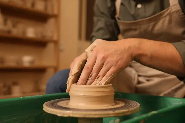 Clay crafting. Man making bowl on potter\'s wheel indoors, closeup