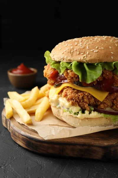 Delicious burger with crispy chicken patty, french fries and sauce on black table, closeup