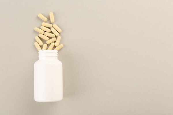 Bottle and vitamin capsules on light background, top view. Space for text