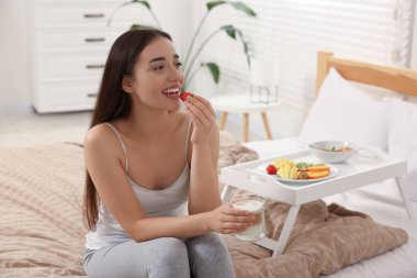 Evdeki beyaz tepsinin yanında kahvaltı eden mutlu genç bir kadın.