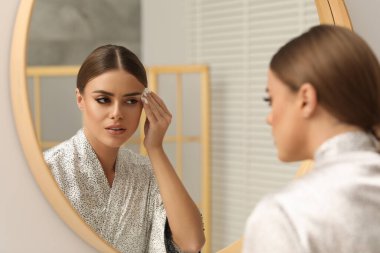 Güzel bir kadın aynanın yanında pamuk yastıkla makyaj yapıyor.