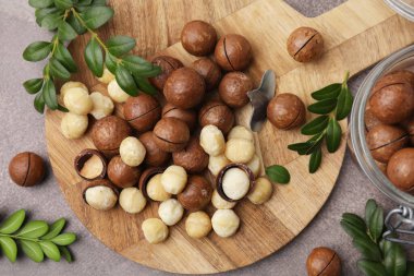 Lezzetli Macadamia fındıkları ve yeşil dallar gri masada, düz yerde.