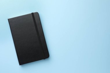 Açık mavi arka planda kapalı siyah defter, üst manzara. Metin için boşluk
