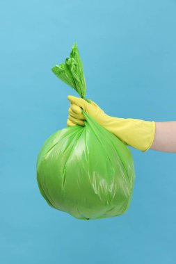 Açık mavi arka planda çöp dolu plastik poşet taşıyan kadın, yakın plan.