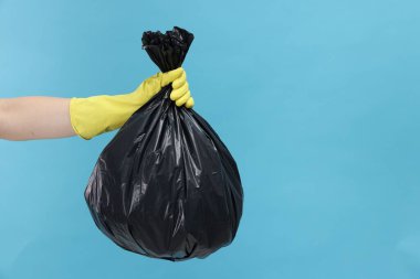 Açık mavi arka planda çöp dolu plastik poşet taşıyan bir kadın, yakın plan. Metin için boşluk