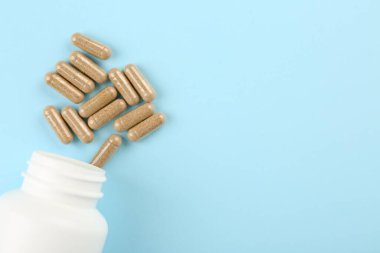 Açık mavi arka planda şişe ve vitamin kapsülleri, üst manzara. Metin için boşluk