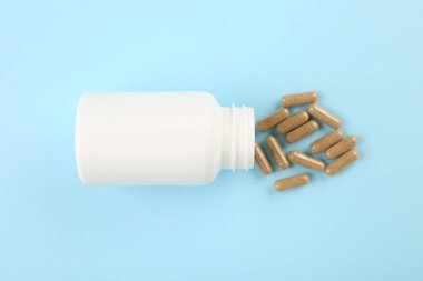 Açık mavi zemin üzerinde şişe ve vitamin kapsülleri, üst görünüm