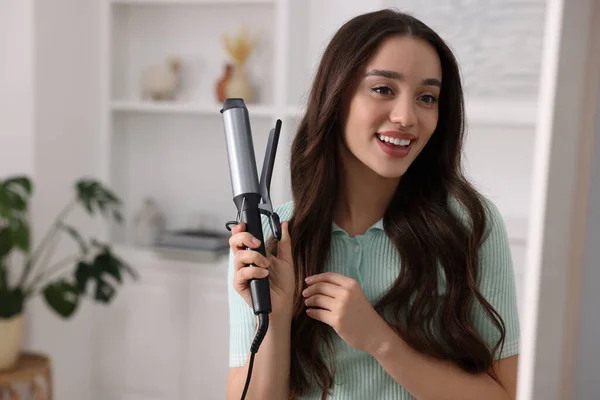 Happy woman with curling hair iron at home