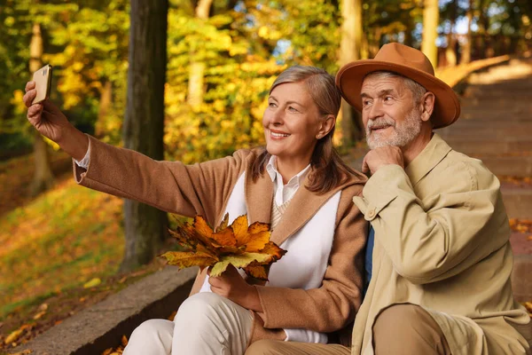 Güz parkında selfie çeken kuru yapraklı sevimli yaşlı çift.