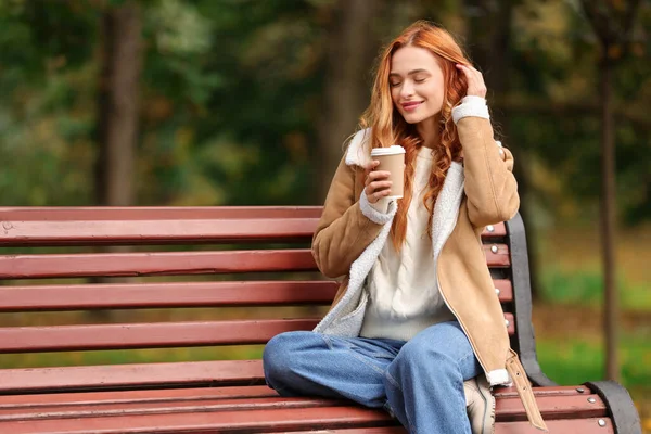 Güz parkında elinde kağıt bardakla bankta oturan güzel bir kadın. Metin için boşluk
