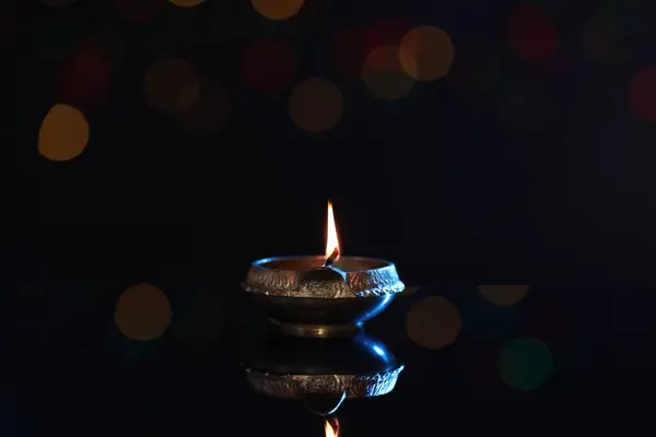 stock image Lit diya on dark background with blurred lights, space for text. Diwali lamp