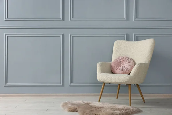 Stylish armchair with pillow and rug near light grey wall indoors. Space for text