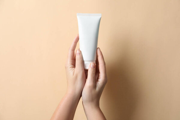 Woman with tube of hand cream on beige background, closeup