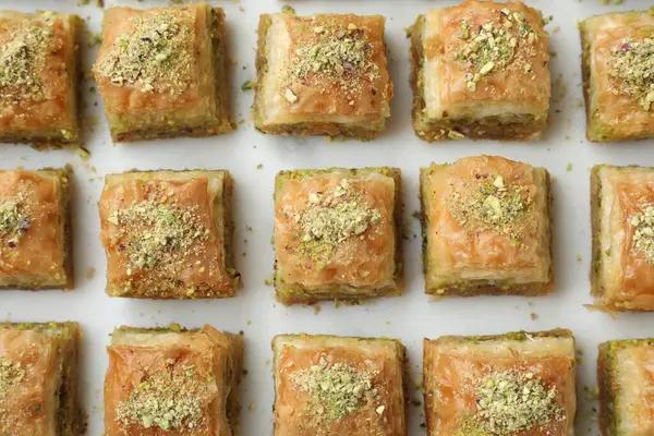 Delicious fresh baklava with chopped nuts on white table, flat lay. Eastern sweets