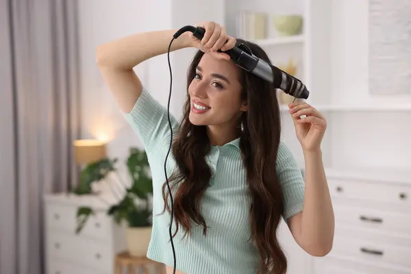 Smiling woman using curling hair iron at home