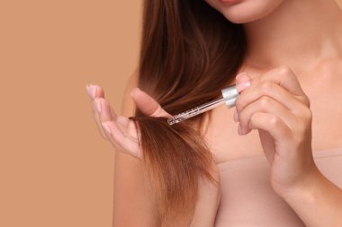 Kadın bej arka plandaki saçlara serum uyguluyor, yakın plan.