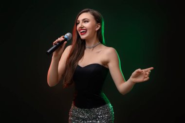 Mikrofonlu duygusal bir kadın. Arka planda renkli ışıklar eşliğinde şarkı söylüyor.