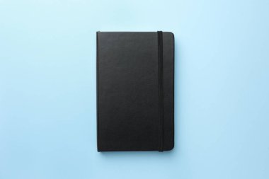 Açık mavi arkaplanda kapalı siyah defter, üst görünüm