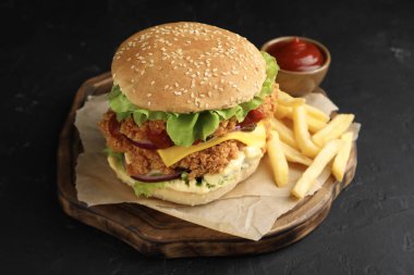 Çıtır tavuk köfteli lezzetli burger, patates kızartması ve siyah masada sos.