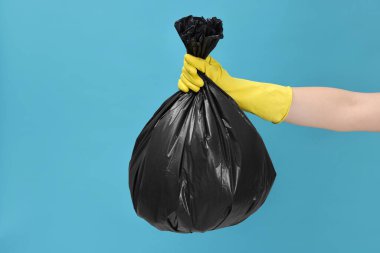 Açık mavi arka planda çöp dolu plastik poşet taşıyan kadın, yakın plan.