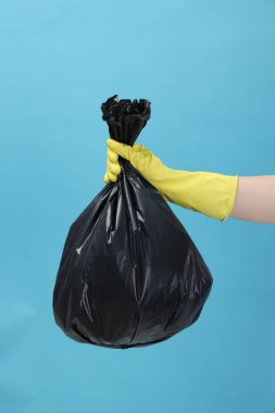 Açık mavi arka planda çöp dolu plastik poşet taşıyan kadın, yakın plan.
