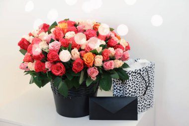 Güzel güller, zarf ve alışveriş çantası beyaz masada.