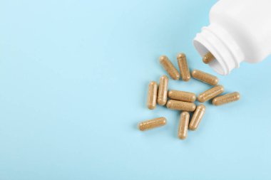 Açık mavi arka planda şişe ve vitamin kapsülleri, üst manzara. Metin için boşluk
