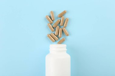 Açık mavi zemin üzerinde şişe ve vitamin kapsülleri, üst görünüm