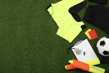 Üniforma, futbol topu ve yeşil çimlerde diğer hakem ekipmanları, düz konum. Metin için boşluk