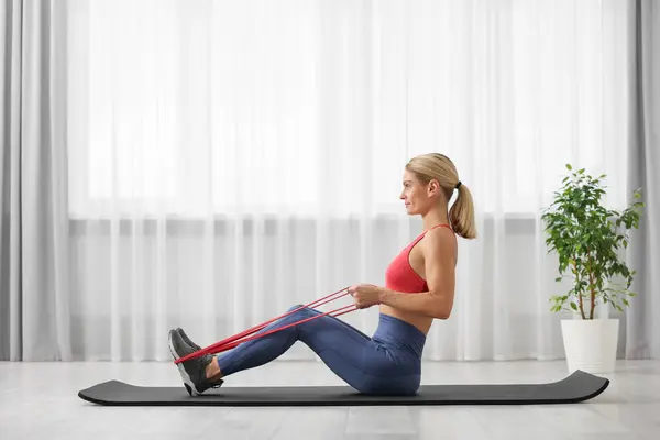 Fit woman doing exercise with fitness elastic band on mat at home