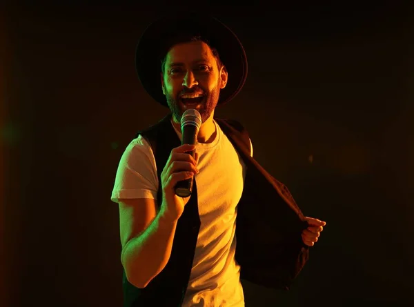 Handsome man with microphone singing in neon lights on dark background