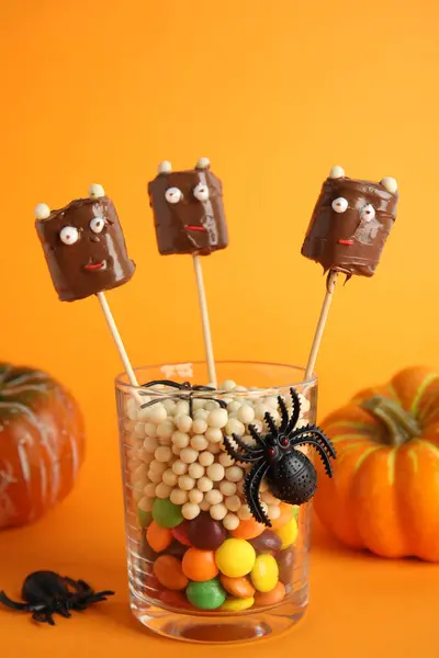 Delicious candies decorated as monsters on orange background. Halloween treat